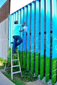 Enrique painting on the border wall in Playas de Tijuana. Photo by: Noemi Ramirez